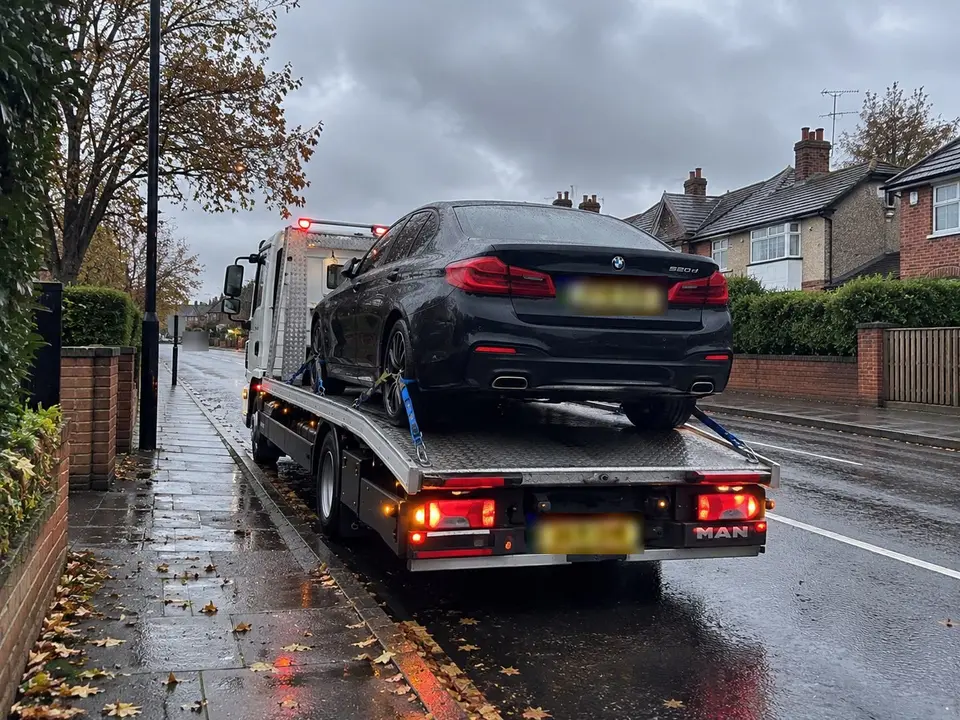 Black BMW saloon strapped onto a recovery truck on a rainy residential street