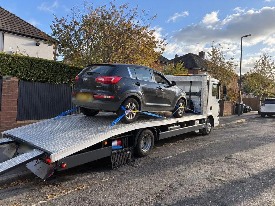 Grey Kia SUV secured with wheel straps on the bed of a recovery truck