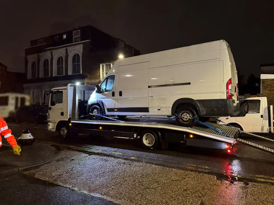 White van being recovered at night on a lit flatbed truck