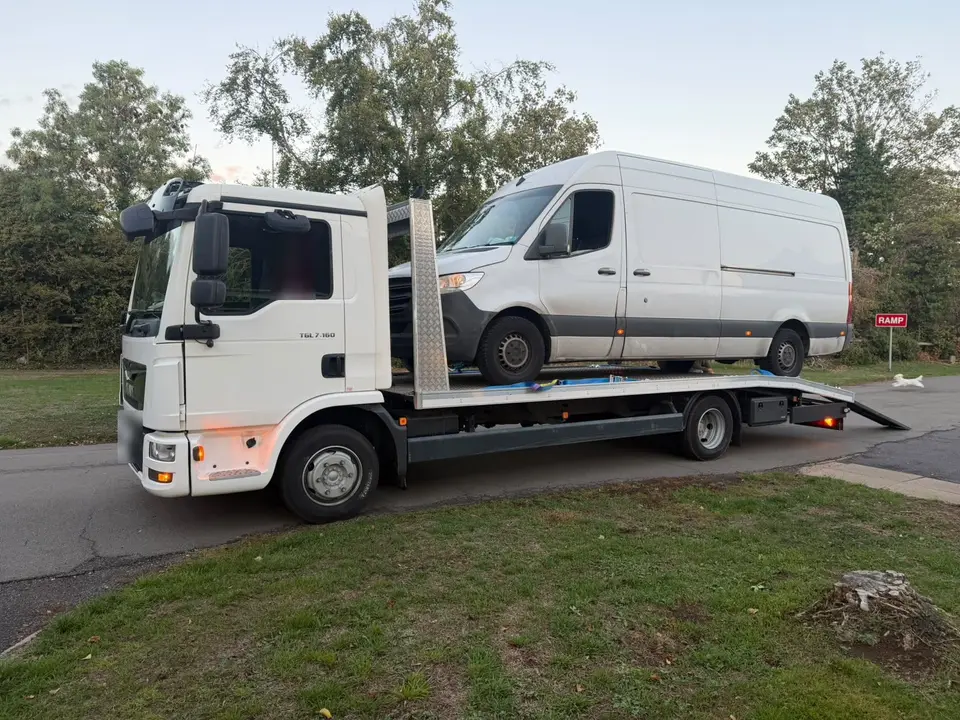 Large white panel van loaded onto a flatbed recovery truck
